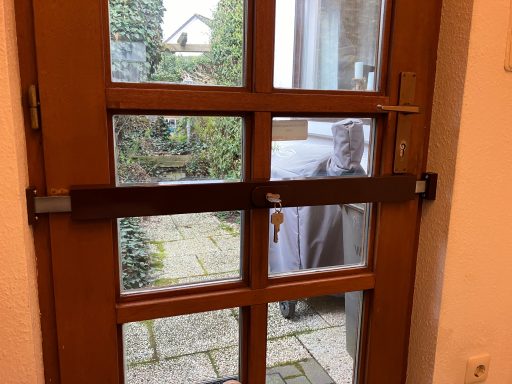 Braune Glastür mit einem Sicherheitsverschluss und Blick auf den Garten.