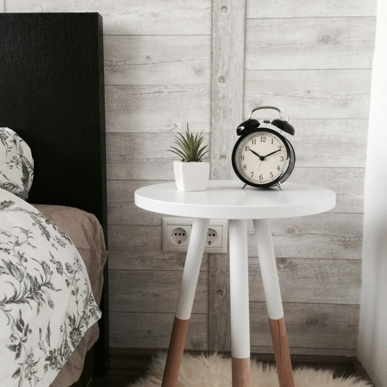 Weißer Nachttisch mit Uhr und Pflanze neben einem Bett in einem modernen Schlafzimmer.