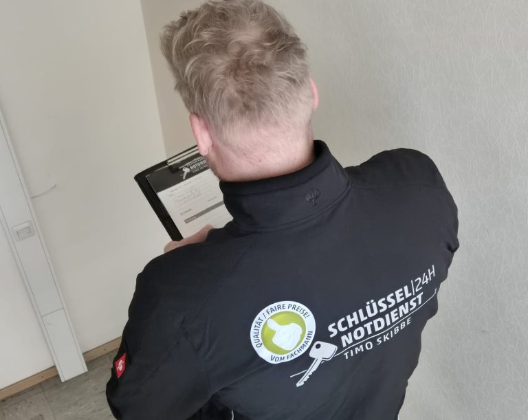 Person mit Jacke im Rückenansicht steht an einer Wand und hält ein Klemmbrett.