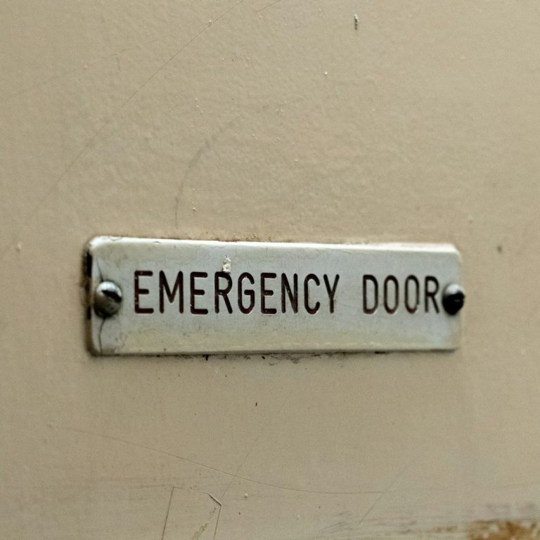 Schild mit der Aufschrift "EMERGENCY DOOR" an einer Wand.
