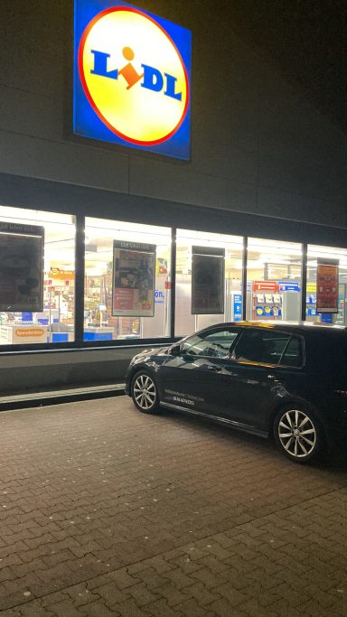 Schwarz glänzendes Auto vor dem Lidl-Supermarkt mit leuchtendem Logo.