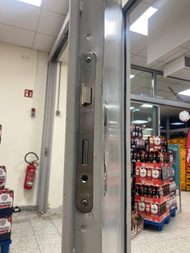 Türschloss an einem Glastürrahmen in einem Supermarkt. Im Hintergrund Getränke-Regale.